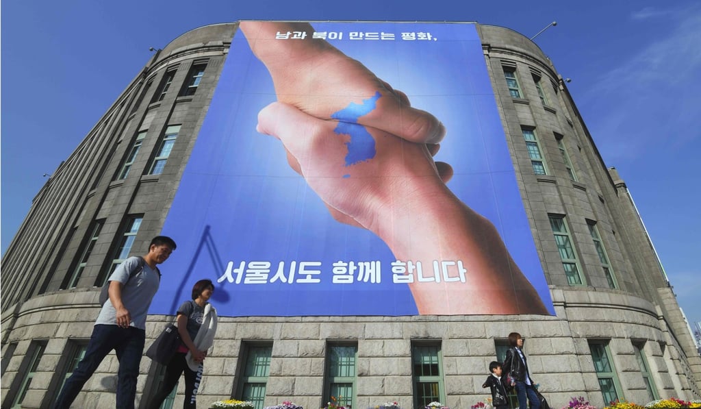 Pedestrians walk past a banner showing two hands clasping, forming the shape of the Korean peninsula, at Seoul City Hall on April 18. The lead-up to the inter-Korean summit in Panmunjom on Friday was accompanied by a publicity blitz promoting efforts to establish peace and unification. Photo: AFP