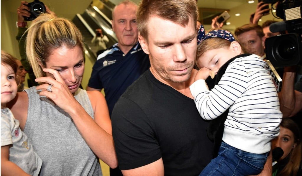 David Warner (centre), his wife Candice and their daughters leaving the airport after arriving back in Sydney from South Africa. Photo: AFP