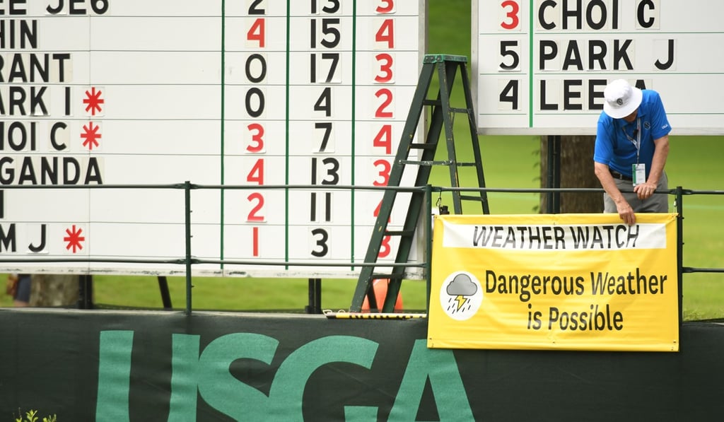 A volunteer adjusts a sign near the scoreboard that advises spectators that inclement weather could be moving over the course during the second round. Photo: USA TODAY Sports