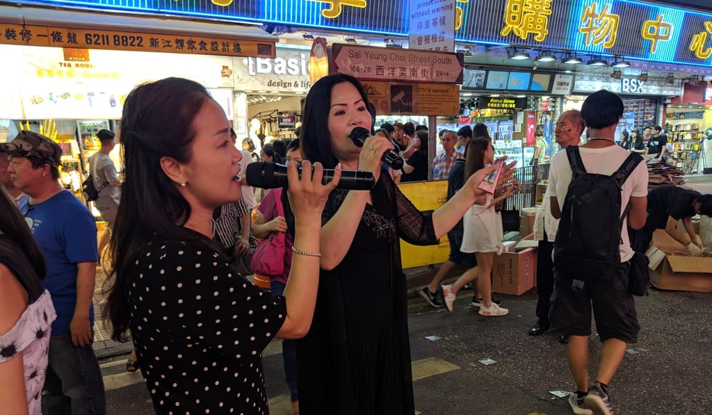 Singer Ling (right) holds cash tips whilst performing on Sai Yeung Choi Street South. Photo: Sum Lok-kei Singer Ling (right) holds cash tips whilst performing on Sai Yeung Choi Street South. Photo: Sum Lok-kei