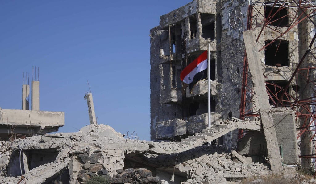 The Syrian flag rises in the middle of damaged buildings in Daraa-al-Balad, an opposition-held part of the southern city of Daraa. Photo: AFP