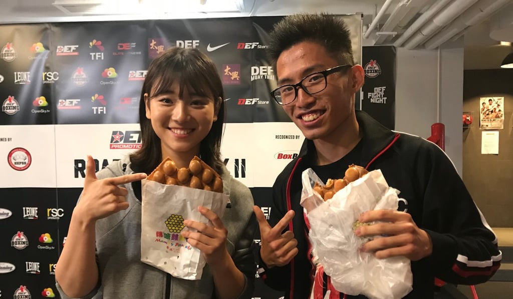 Newly crowned WBC ABCO light flyweight champion Raymond Poon presents Nanako Suzuki with her favourite Hong Kong snack at the DEF Boxing Club in Sheung Wan.