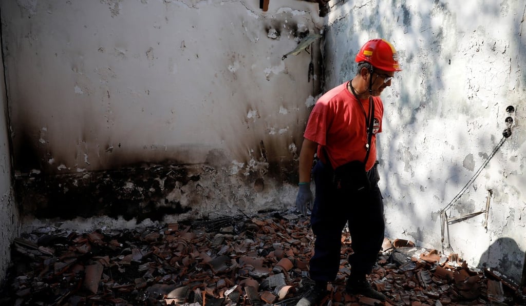 A member of a rescue team searches inside a destroyed house following a wildfire at the village of Mati on Wednesday. Photo: Reuters