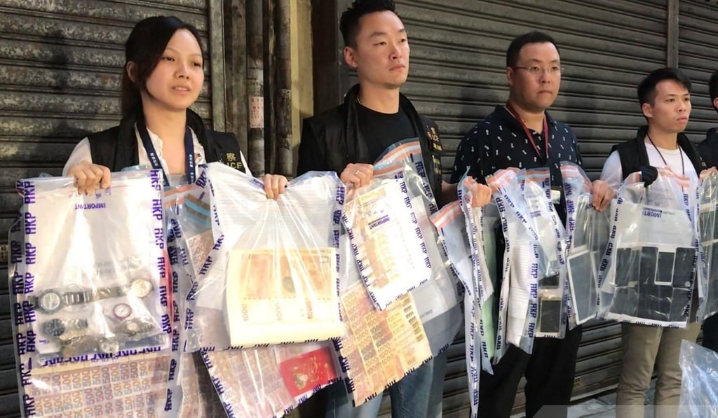 Officers from the Kowloon West regional intelligence unit, which conducted the raid, with some of the fake notes and stolen goods seized. Photo: RTHK Officers from the Kowloon West regional intelligence unit, which conducted the raid, with some of the fake notes and stolen goods seized. Photo: RTHK