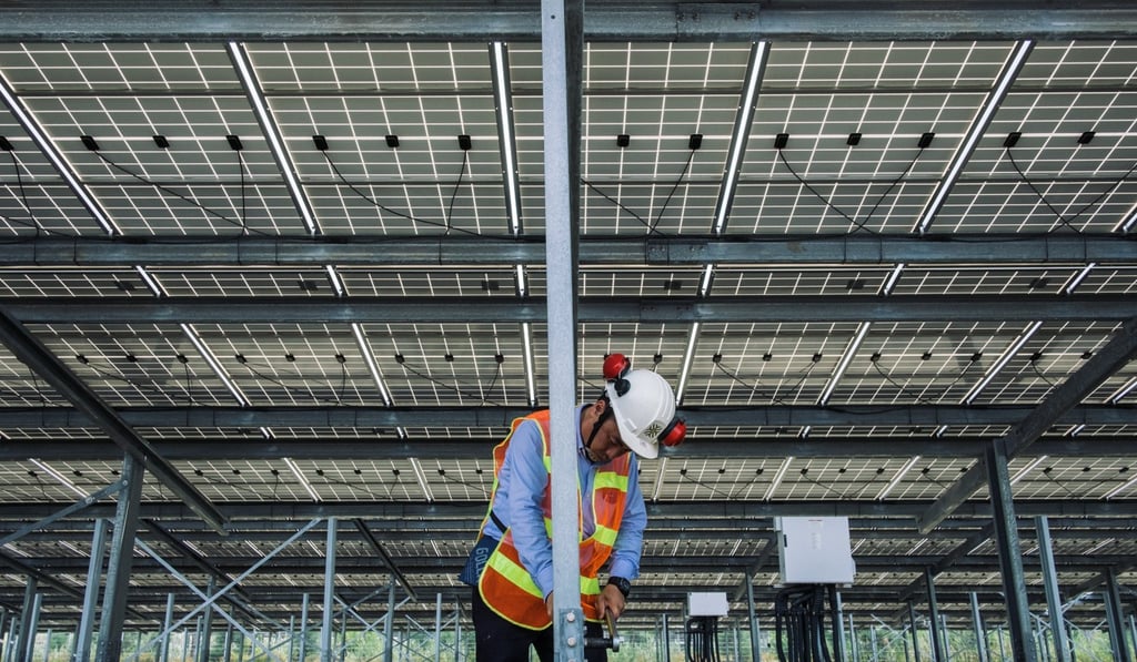 A worker tightens a screw under solar panels at a Vena Energy solar-power installation. Photo: Bloomberg