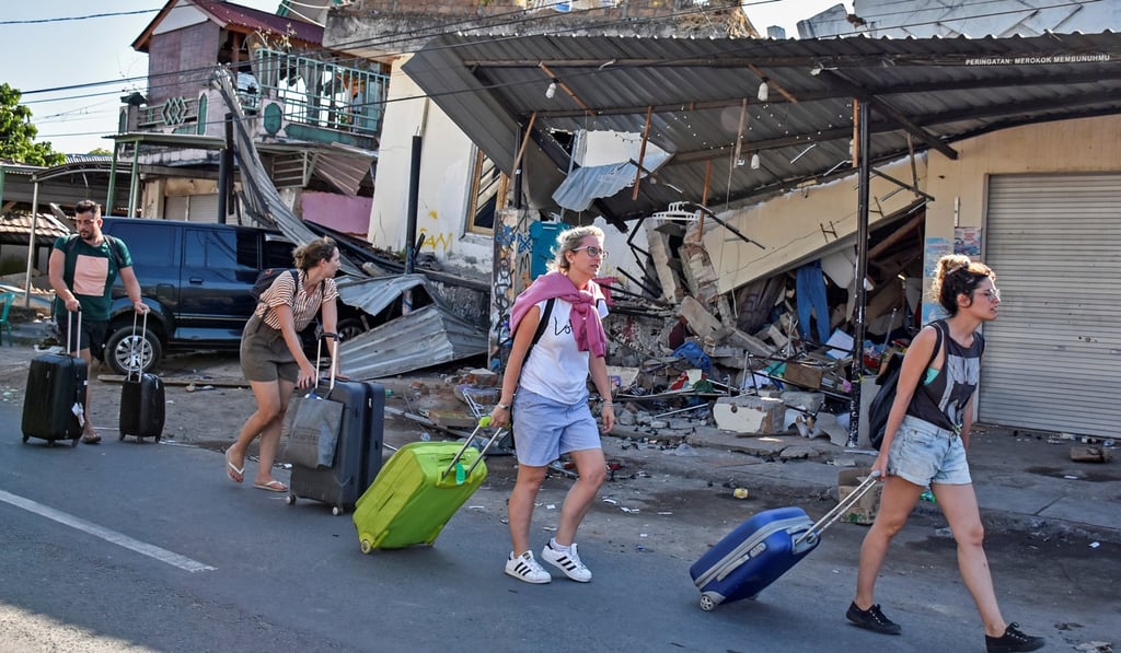 Foreign tourists pull their suitcases as they walk past damaged buildings following a strong earthquake in Pemenang, Lombok, this week. Thousands left the Indonesian island after the disaster, which left at least 108 people dead. Photo: Antara Foto/Ahmad Subaidi/Reuters
