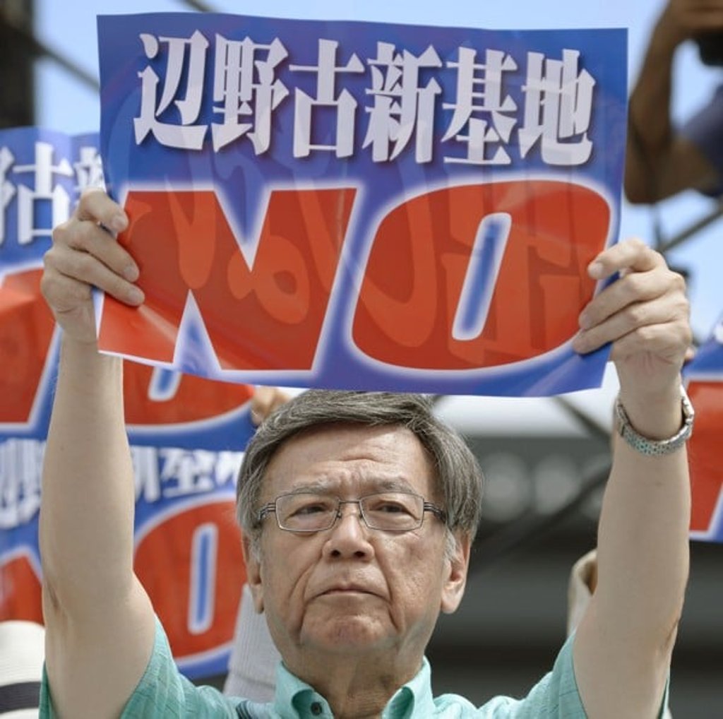 Onaga holding a sign saying ‘No new US base at Henoko’ at a rally in Naha, Okinawa. Photo: Kyodo/AP)