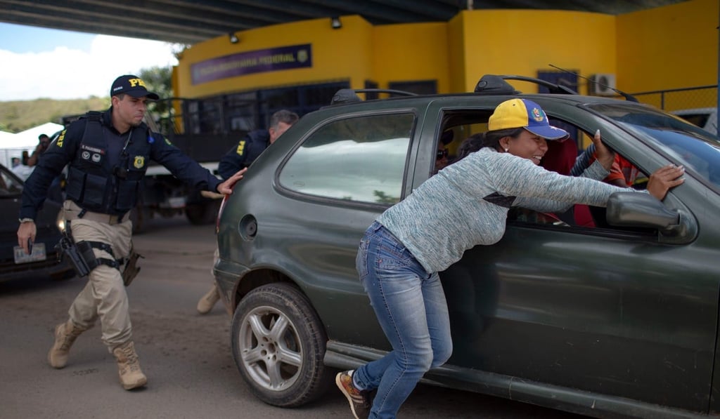 A Brazilian police officer helps Venezuelans push their car after it broke down while leaving the Brazilian Migration Office in the border city of Pacaraima, Roraima State, Brazil. Photo: AFP