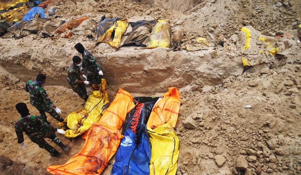 Indonesian military personnel place bodies in a grave during a mass burial in Palu. Photo: EPA