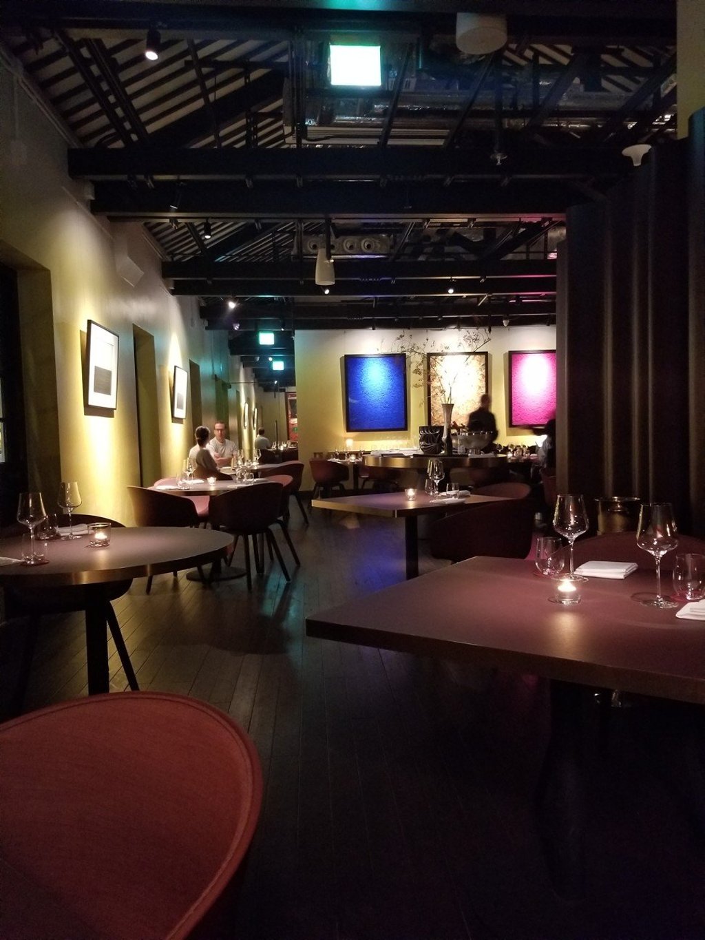 The main dining area features high ceilings and light walls decked with colourful modern artwork illuminated by spotlights.