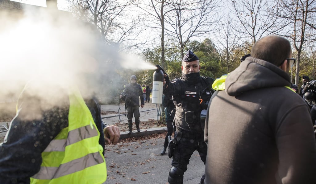 A police officer uses tear gas against a man wearing a yellow vest in Paris. Photo: EPA