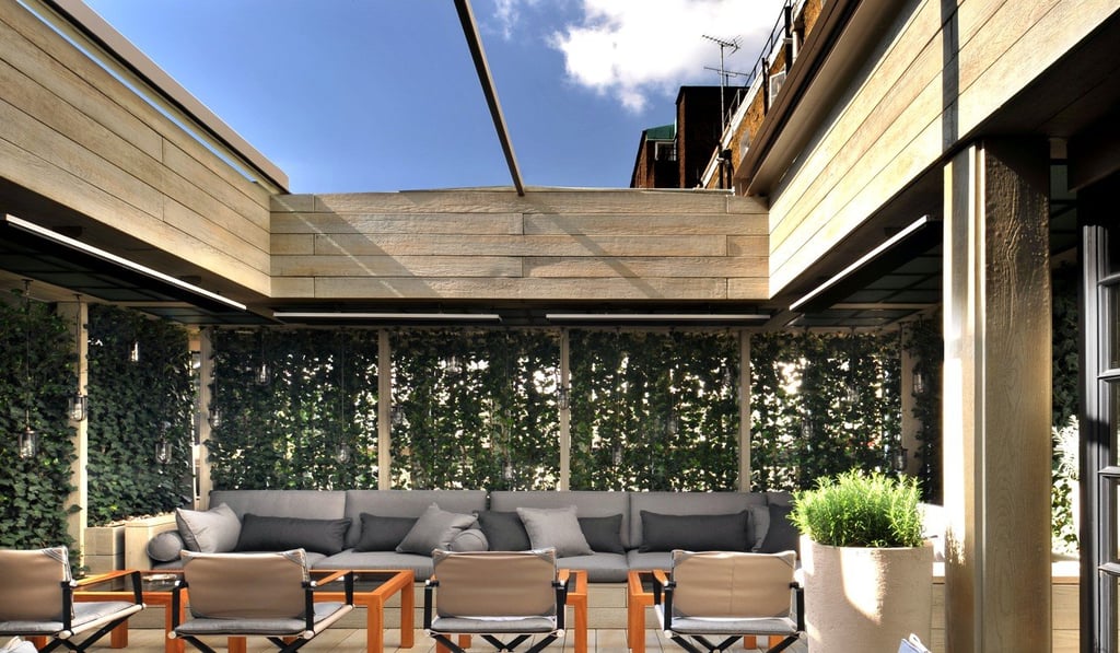 Wooden flooring and detailing and muted grey and black fabrics on seating help to create an inviting outdoor seating area at the boutique hotel, The Hari, in London.