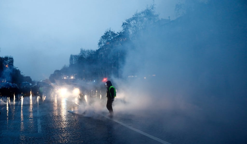 A protester wearing a yellow vest stands amid smoke of tear gas as he faces French riot police during a demonstration against rising costs of living they blame on high taxes on the Champs-Elysees Avenue in Paris, on December 15, 2018. Photo: AFP