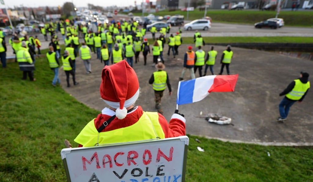 A Yellow vest protester dressed as Santa Claus with a sign reading “Macron stole the gifts of our children” waves a French flag during a protest close to highway access in Saint Saturnin, near Le Mans, northwestern France. Photo: AFP