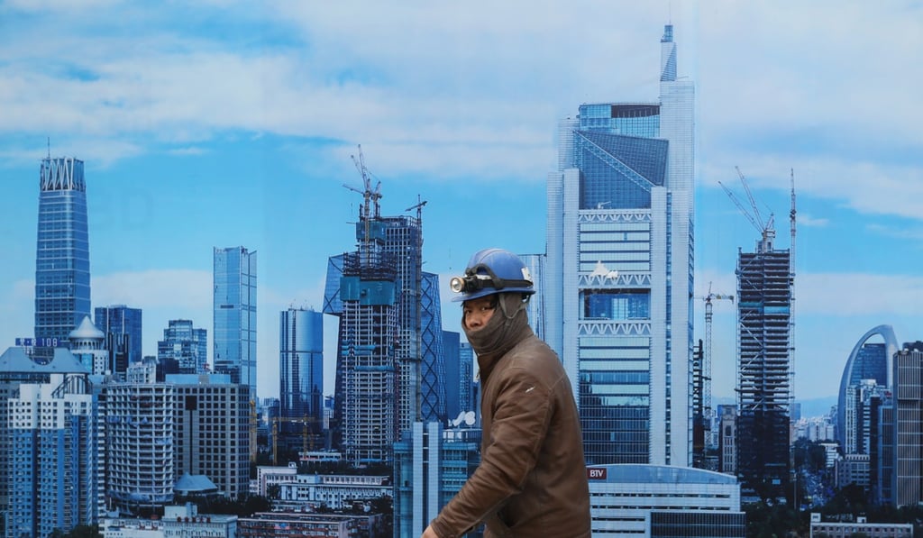 A worker walks past a poster outside a construction site in Beijing. The price-to-income ratio in the city is around 23 – meaning the average household would have to work for more than two decades, without spending, to buy a home. Photo: EPA-EFE