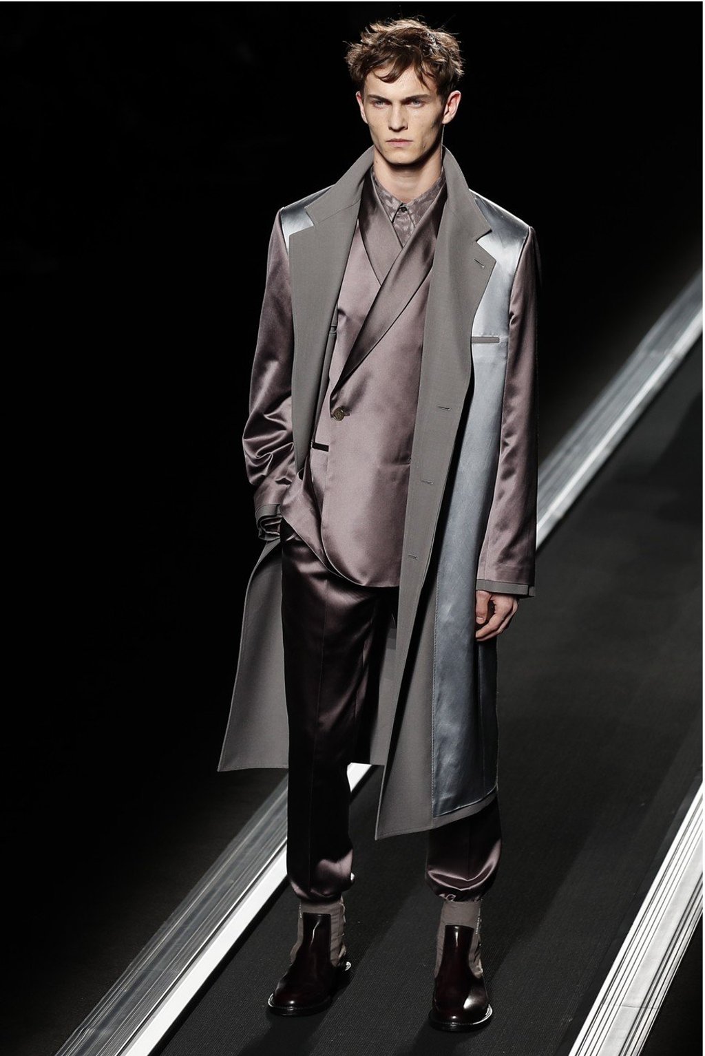 A model stands on the conveyor-belt catwalk as he presents a silky brown men’s suit and grey and brown overcoat – with the suit trousers tucked into a pair of boots – designed by Kim Jones during the Dior fall/winter 2019-20 show at Paris Fashion Week. Photo: EPA-EFE