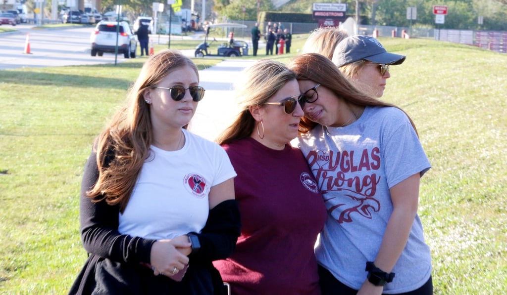 Cheryl Rothenberg embraces her daughters Emma and Sophia as they look at a memorial on the one-year anniversary of the massacre that killed 17 people at Marjory Stoneman Douglas High School in Parkland, Florida. Photo: Reuters