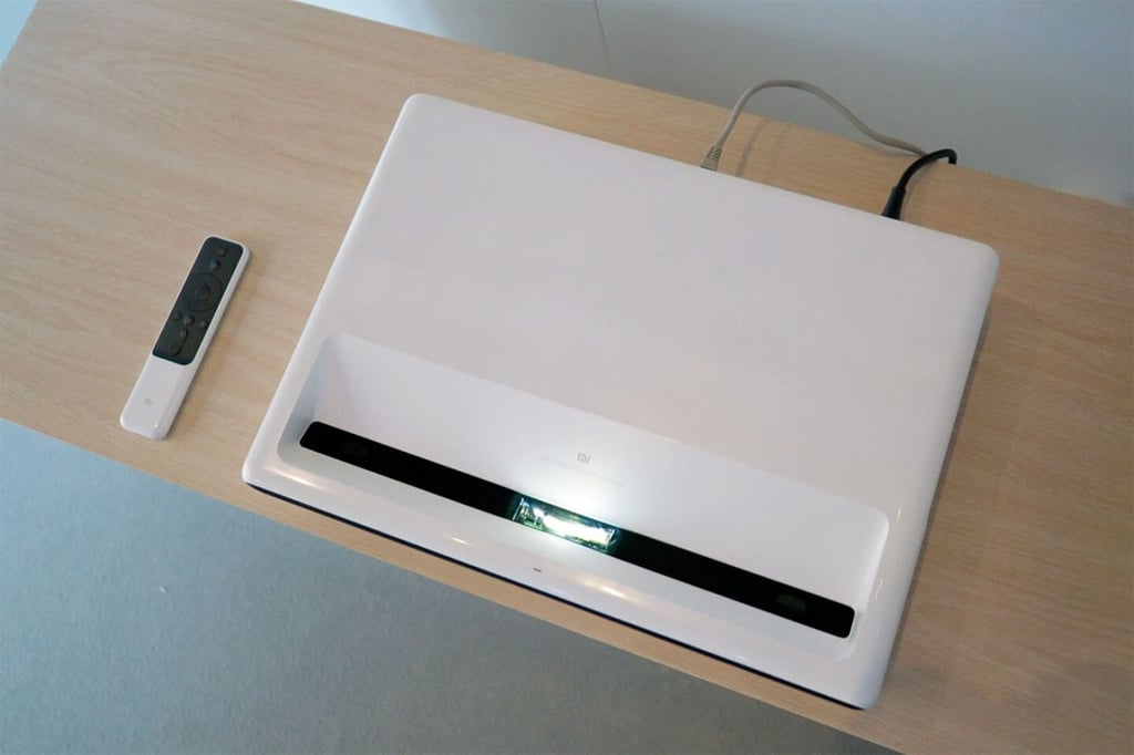 The Mi Laser Projector has a rectangular design with a black speaker grille in front.