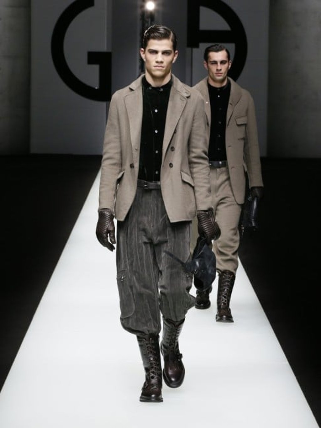 Beige double cashmere jacket worn over forest green velvet shirt and grey pleated velvet cargo trousers. Accessorised with black sheepskin-lined leather aviator hat, and dark brown quilted nappa leather gloves.