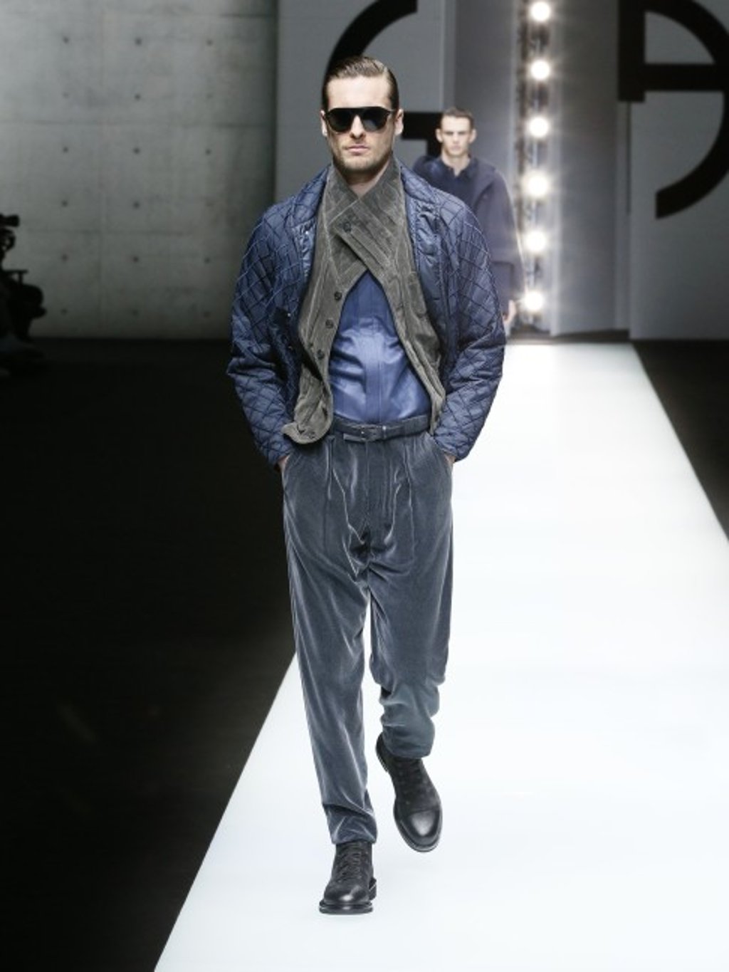 Blue jacket in check-embroidered technical canvas worn with grey pleated velvet waistcoat, blue micro-woven cotton shirt, and navy blue flocked velvet trousers.