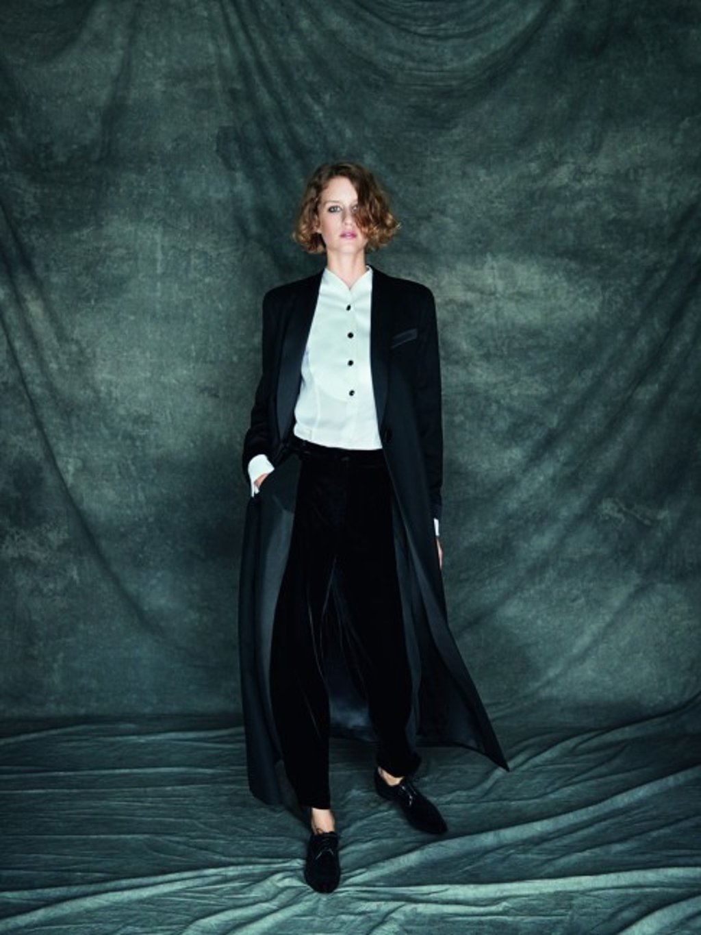 Long black coat in cashmere and satin worn over white silk shirt and black velvet trousers.