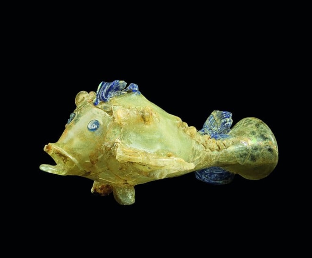 The fish is made from blown glass, with fins drawn out from glass strips. The usage of this glass fish is uncertain but the remnant of fragrance oil left on the interior wall suggests that they were vessels for holding essence oil or ointment