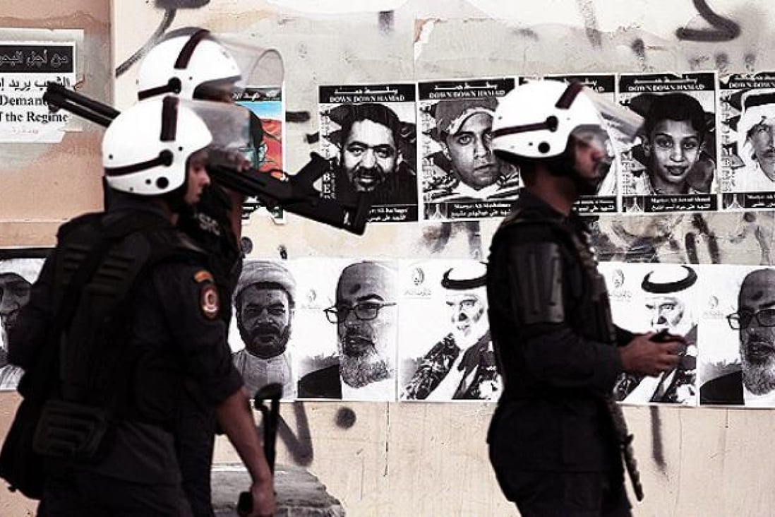 Bahraini riot policemen search for anti-government protesters during clashes in Sitra on Monday. Pictures of jailed political leaders behind last year's uprising and people killed in the ensuing unrest are plastered on the wall. Photo: AP