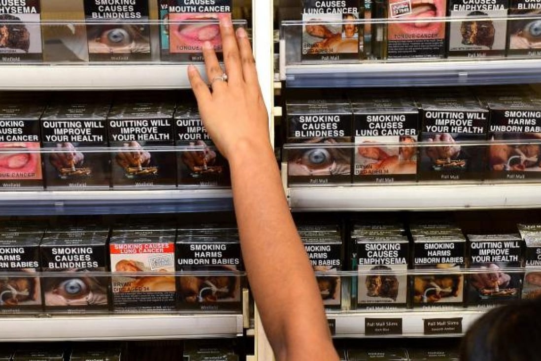 An employee in a bookshop in Australia adjusts packaged cigarettes which have to be sold in identical olive-brown packets. Photo: AFP