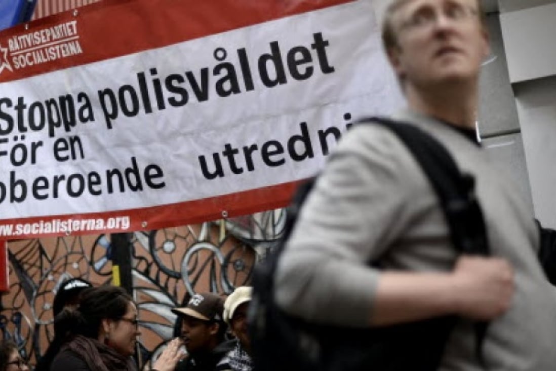 A man passes by a banner reading "Stop police violence for an independent investigation" during a demonstration against police violence and vandalism in the Stockholm suburb of Husby. Photo: AFP