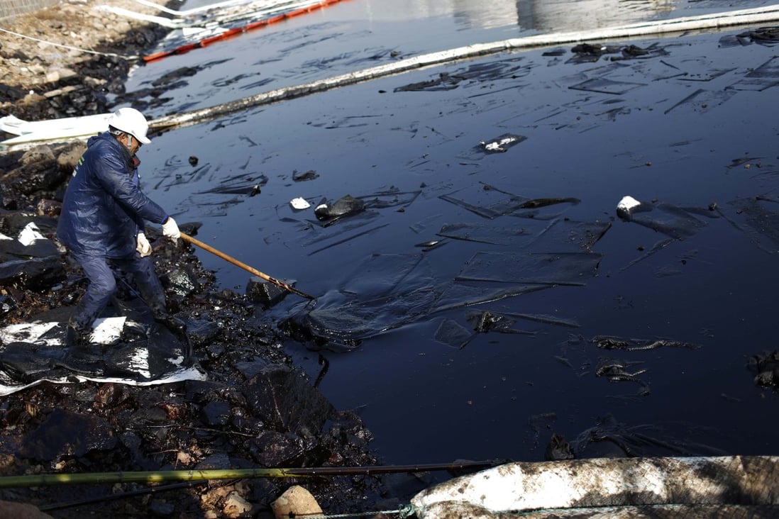 Worker cleans up leaked oil after last week's explosion of a Sinopec Corp oil pipeline in Huangdao. Photo: Reuters