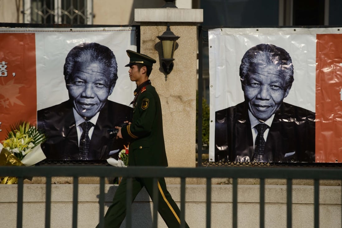 A paramilitary policeman walks past portraits of the late Nelson Mandela outside the South African embassy in Beijing. Photo: AFP