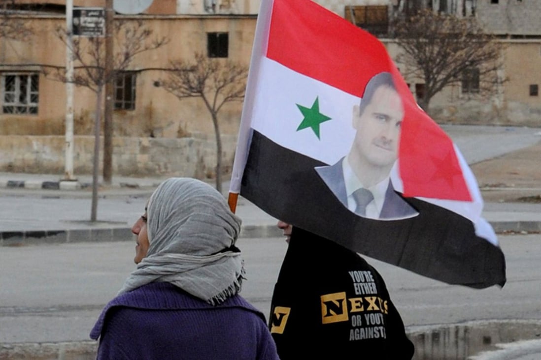 A Syrian woman holds her national flag decorated with a picture of President Bashar al-Assad in a town north of Damascus. Photo: AFP