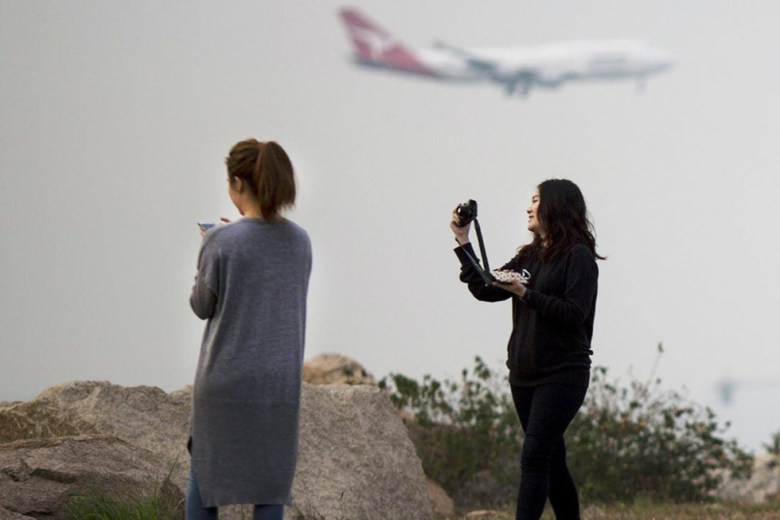 Two women take photographs from a vantage point near Hong Kong's airport as a Qantas Airways jet comes in to land. Photo: Bloomberg