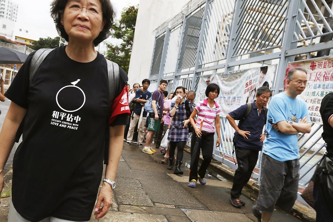 An Occupy Central volunteer outside a polling station looks on as citizens line up to vote for the civil referendum. Photo: Reuters