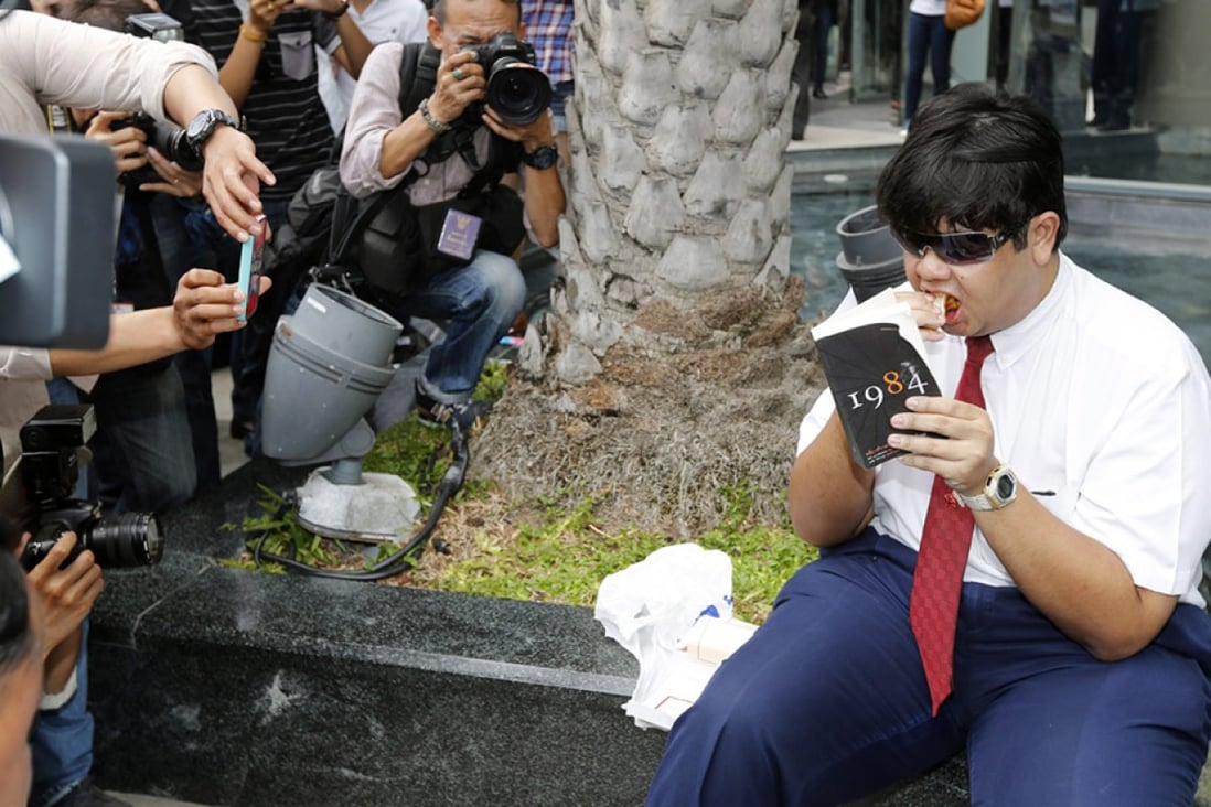 A Thai anti-coup protester eats a sandwich as he reads a book as a sign of protest outside a shopping centre in Bangkok. Photo: EPA