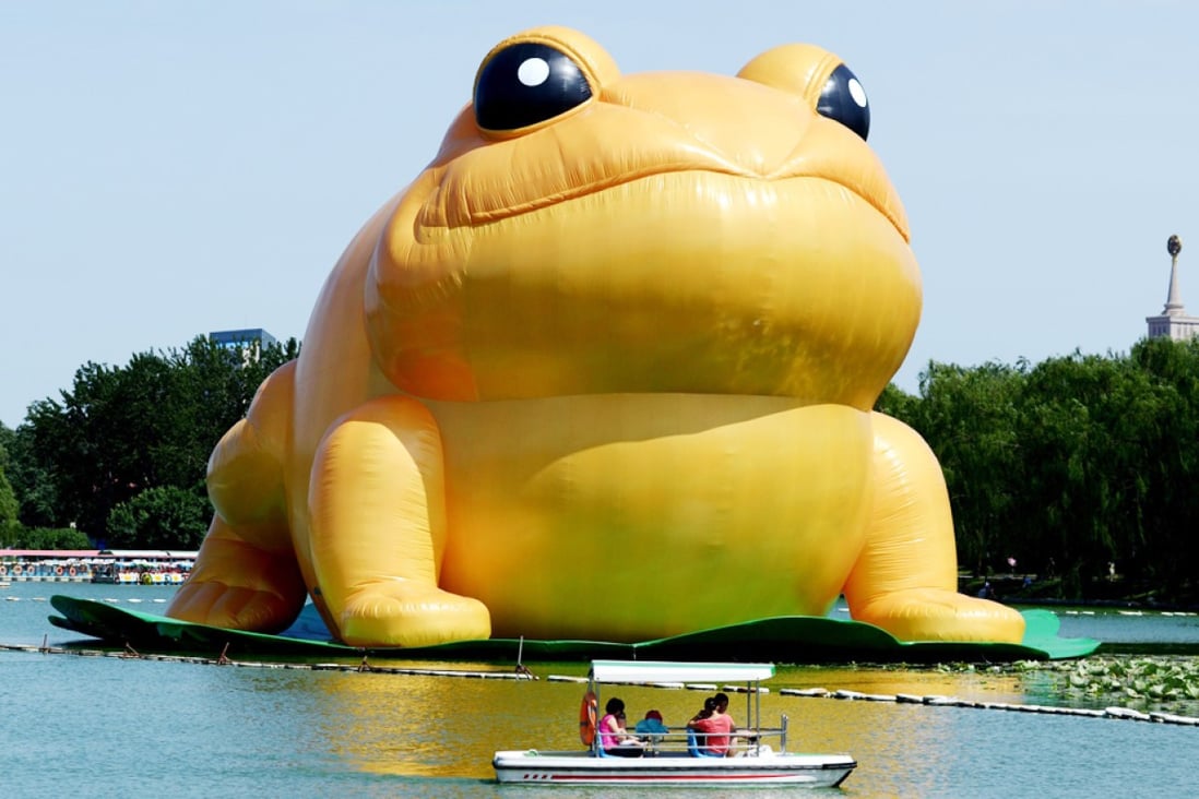 People ride in a boat before the 22-metre tall inflatable toad displayed at Yuyuantan park in Beijing. Photo: AFP