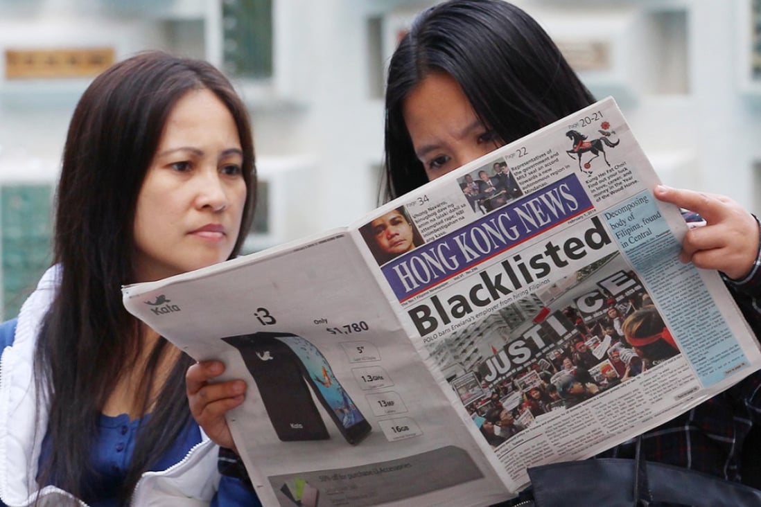Two foreign domestic helpers read a newspaper as they gather near Chater Garden in Central. Photo: Nora Tam