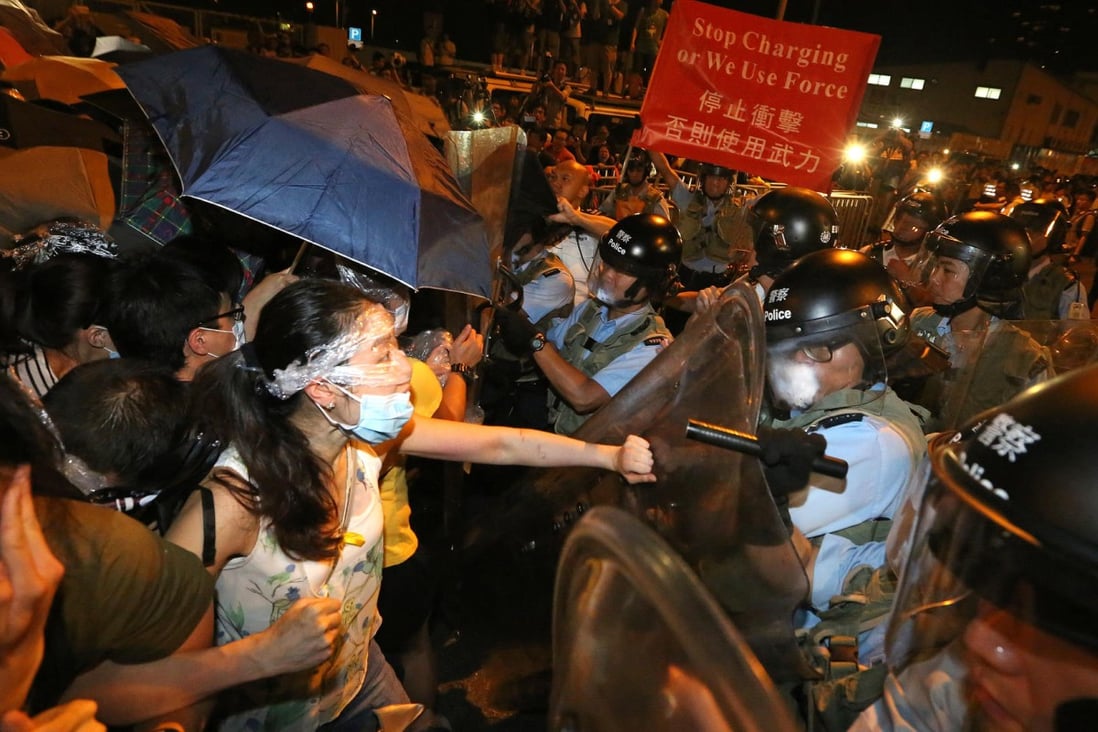 Protesters, mostly students, push back as police charge in with anti-riot gear and pepper spray to remove them from outside government headquarters, and remain defiant. 