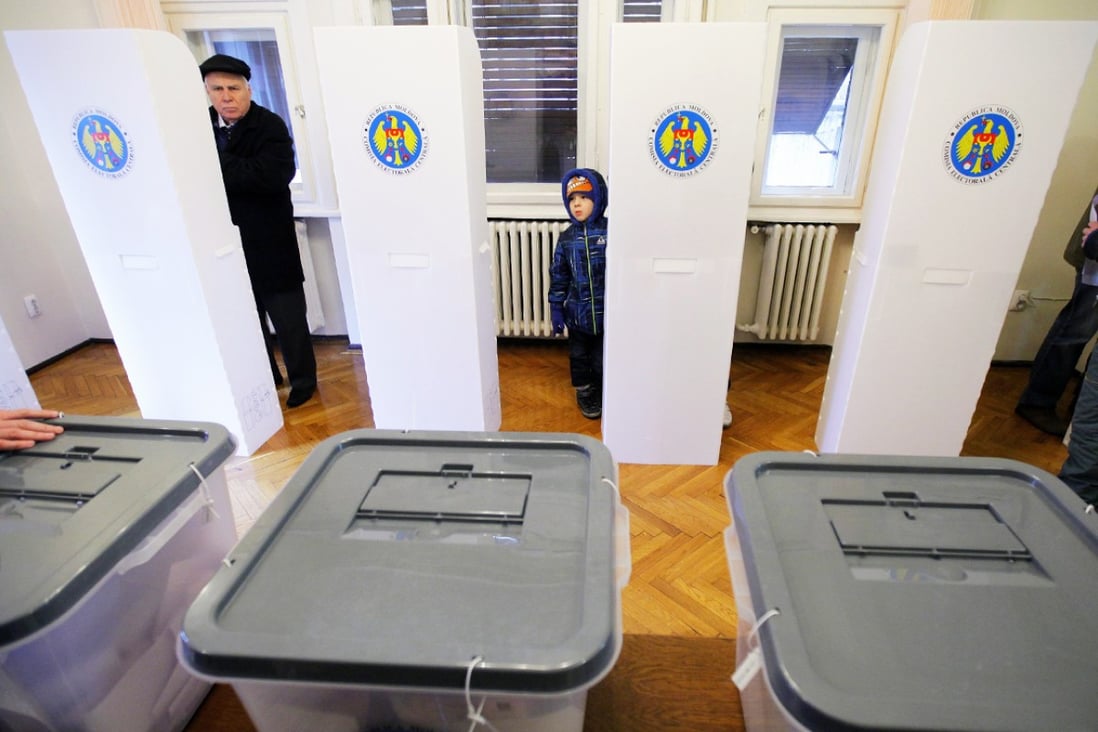 A Moldovan man (left) votes while being watched by a young boy during  Moldova's parliamentary elections, at a polling station organised at Molodva's embassy in Bucharest. Photo: EPA