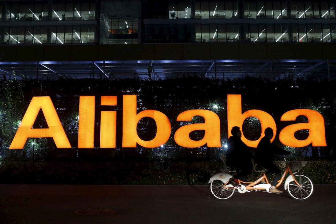 People ride a tandem bike past the Alibaba logo. Photo: Reuters