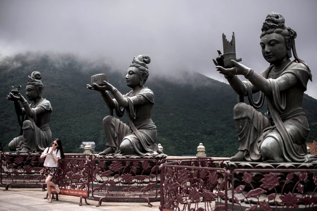 A tourist poses next to statues near the Po Lin Monastery on the outlying island of Lantau in Hong Kong on June 9, 2015. Photo: AFP