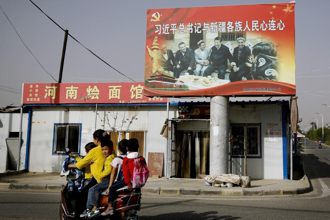 An Uygur woman on a scooter fetches school children as they ride past a picture of China’s President Xi Jinping joining hands with a group of Uygur elders in 2018. Photo: AP