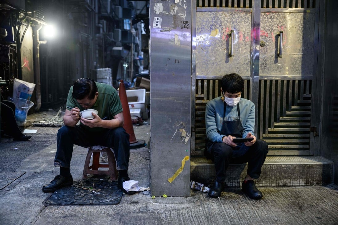 A man eats dinner in an alley as another man checks his phone in Hong Kong on January 4. Photo: AFP 