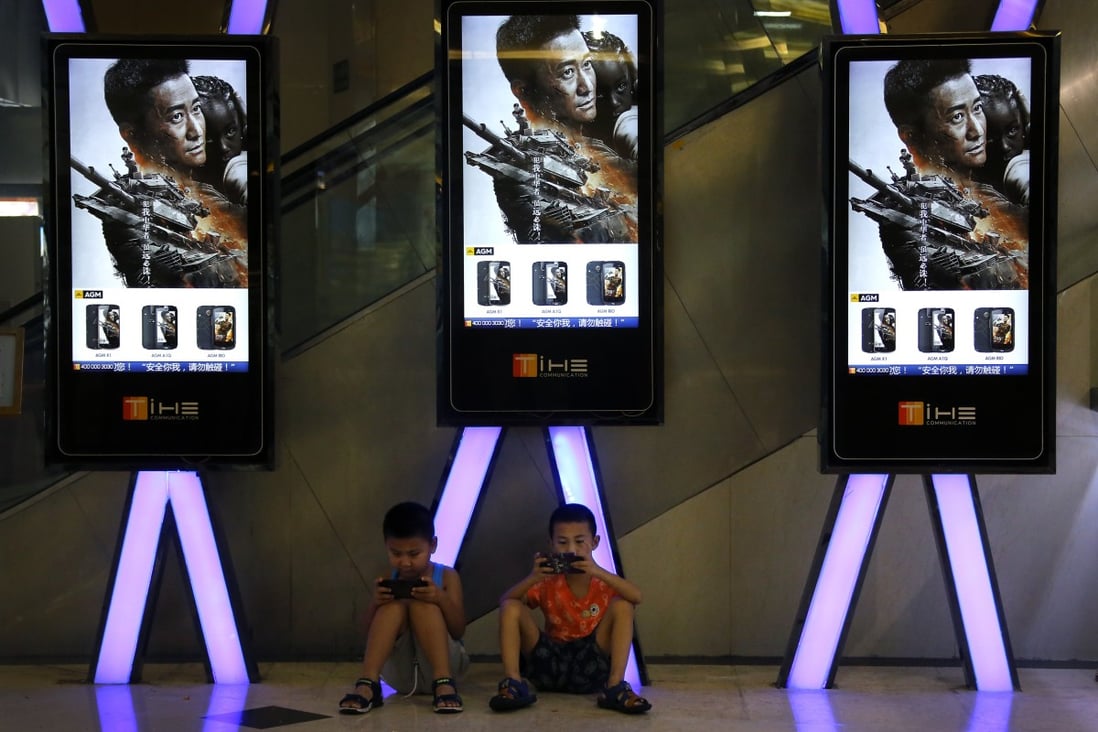 Children use smartphones near monitors displaying a still from Chinese action movie “Wolf Warrior 2” at a cinema in Beijing in August 2017. A new tone of aggression has earned Chinese diplomats the title of “wolf warriors”, after the Rambo-like blockbuster film. Photo: AP 