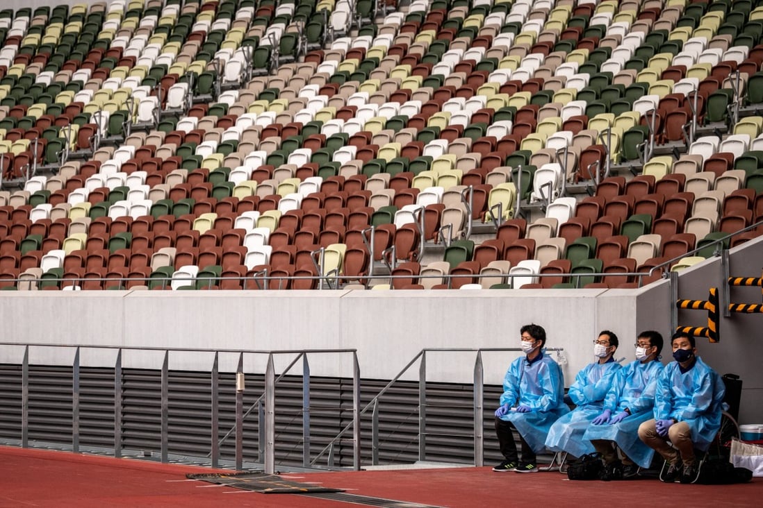Staff members in protective clothing and masks stand by next to empty seats during a para-athletics test event for the 2020 Tokyo Olympics at the National Stadium in Tokyo on May 11, 2021.  Photo: AFP