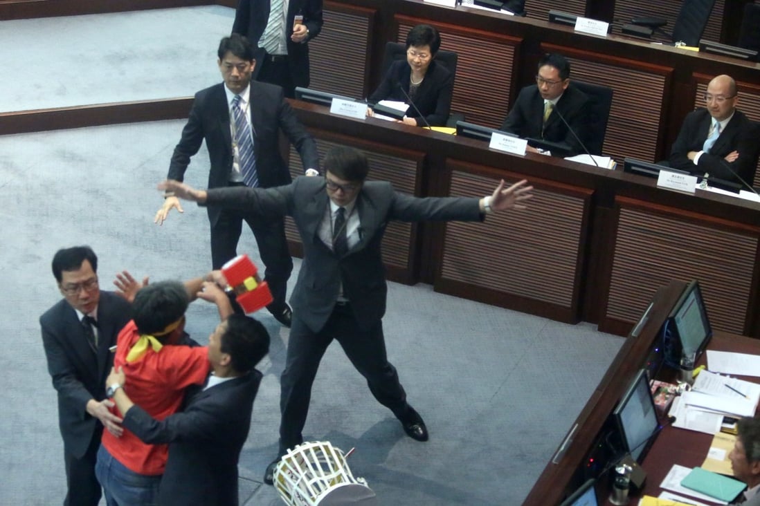 Leung Kwok-hung, in red, is stopped by security guards as he tries to throw a plastic hammer towards then chief secretary Carrie Lam Cheng Yuet-ngor (seated far left) during a meeting on proposed electoral reforms, at the Legislative Council in Hong Kong on July 15, 2014. Photo: Sam Tsang