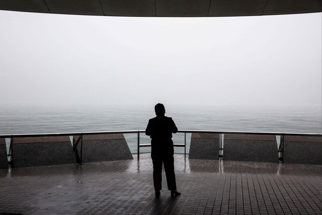 A woman looks out over Victoria Harbour while heavy rain obscures the Hong Kong skyline on July 20. Even Hong Kong’s wildly excessive quarantine rules seem to reflect an inward attitude which should be alien to an international city. Photo: AFP