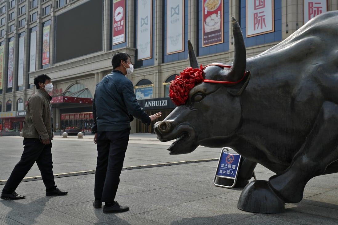 A man wearing a protective face mask touches the investment icon bull statue on display outside a mall in Beijing in March 2020. Photo: AP