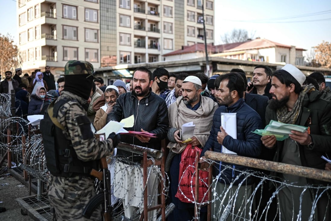 A Taliban fighter inspects documents of people queuing to enter the passport office in Kabul, Afghanistan, on December 18. Photo: AFP