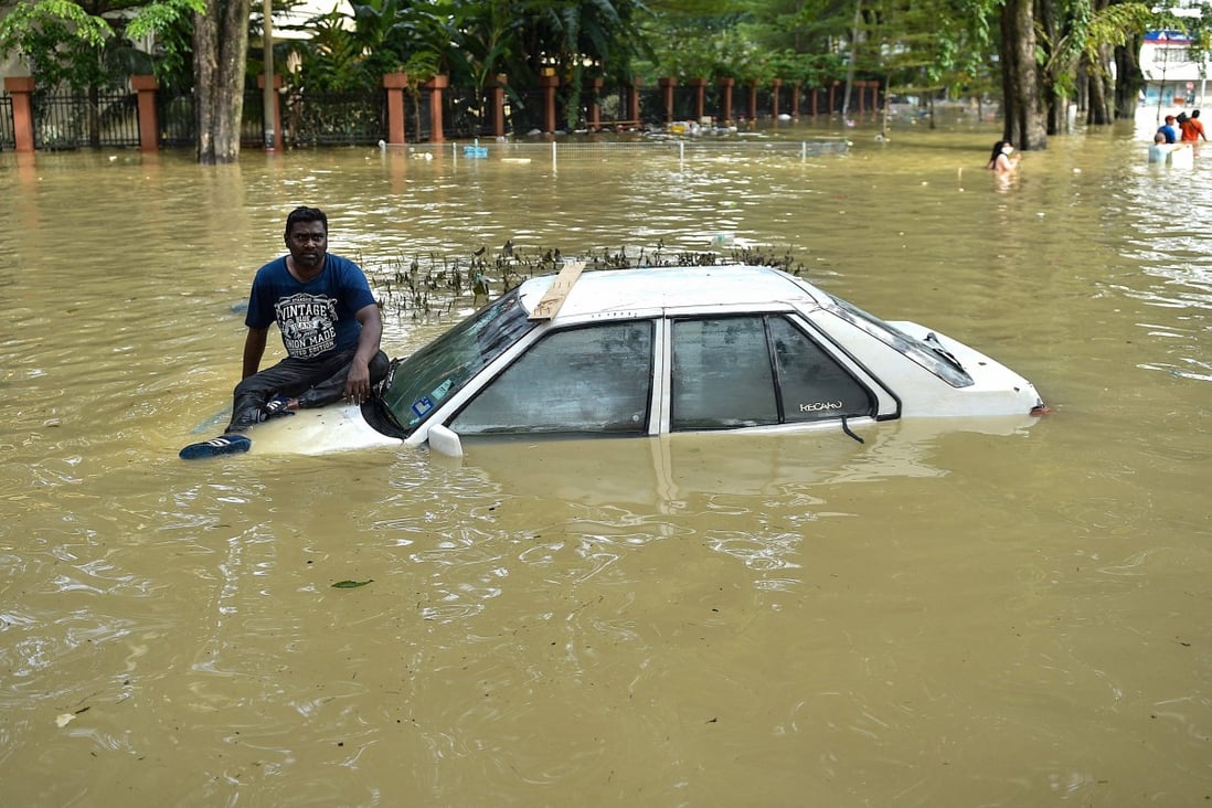 A man sits on the bonnet of a car as he waits to be evacuated by a rescue team in Shah Alam, Selangor, on December 20 after Malaysia experienced some of its worst flooding in years. Photo: AFP